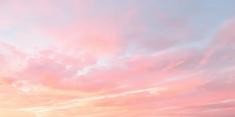 Pastel sky with soft fluffy clouds in pink peach and pale blue at sunrise or sunset