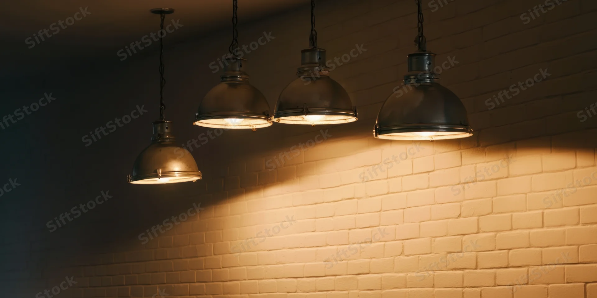 Four industrial pendant spotlights hanging from ceiling casting warm glow on brick wall