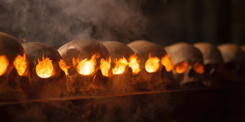 Row of skulls with flames burning in eye sockets in smoky dim setting