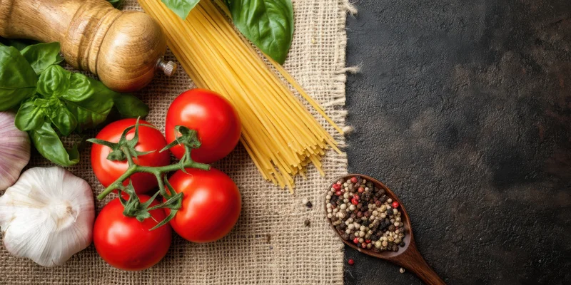 Tomatoes on the vine with spaghetti, basil, garlic, pepper and wooden spoon arranged on burlap and dark surface
