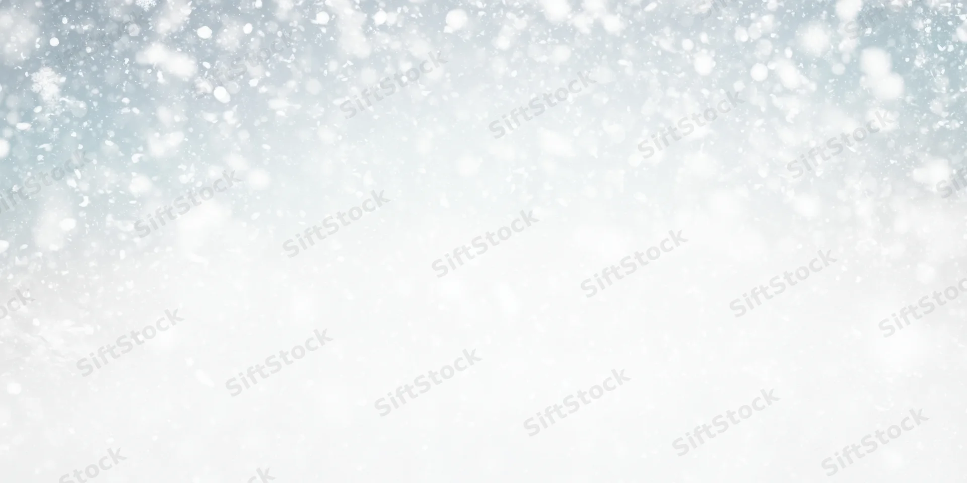 Soft snowfall drifting across a white winter sky with blurred bokeh background