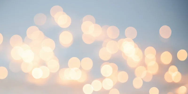 Warm fairy lights creating a soft dreamlike bokeh against a pale sky background