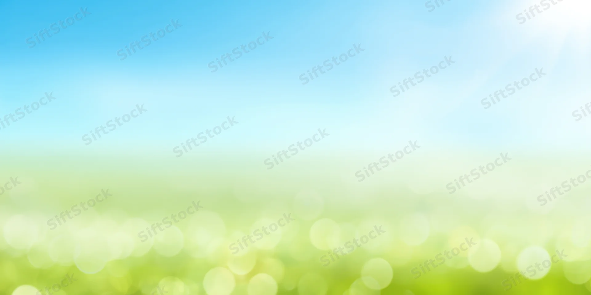Soft sunlit gradient landscape with bright blue sky fading into green field and bokeh lights