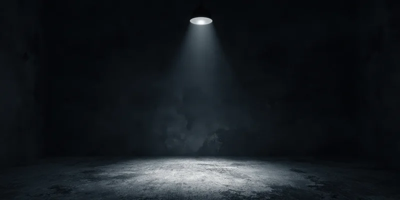 Empty stage illuminated by a single overhead spotlight in a dark industrial room