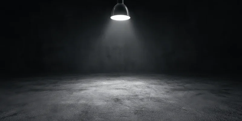Empty stage illuminated by a single overhead spotlight on a concrete floor