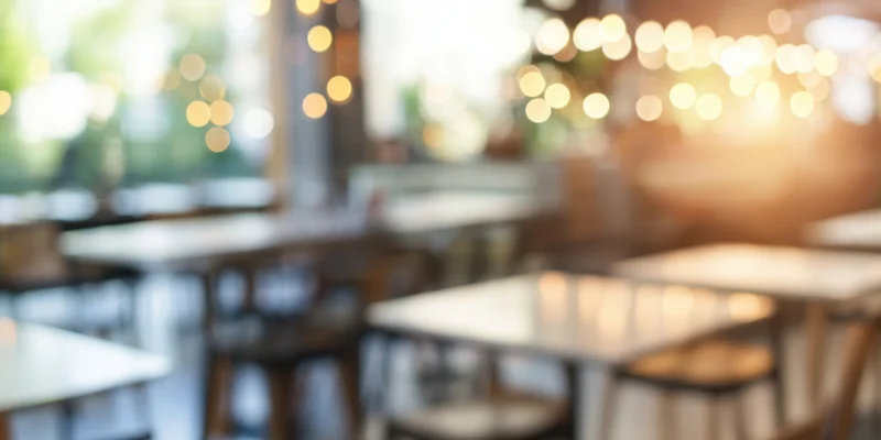 Blurred interior of a modern cafe with tables and chairs under warm sunlit lighting
