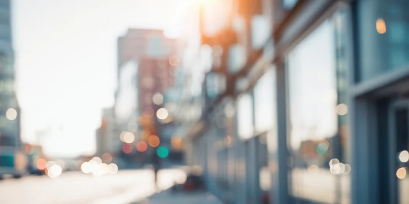 Sunlit urban street with glass-fronted buildings and soft bokeh lights in the background