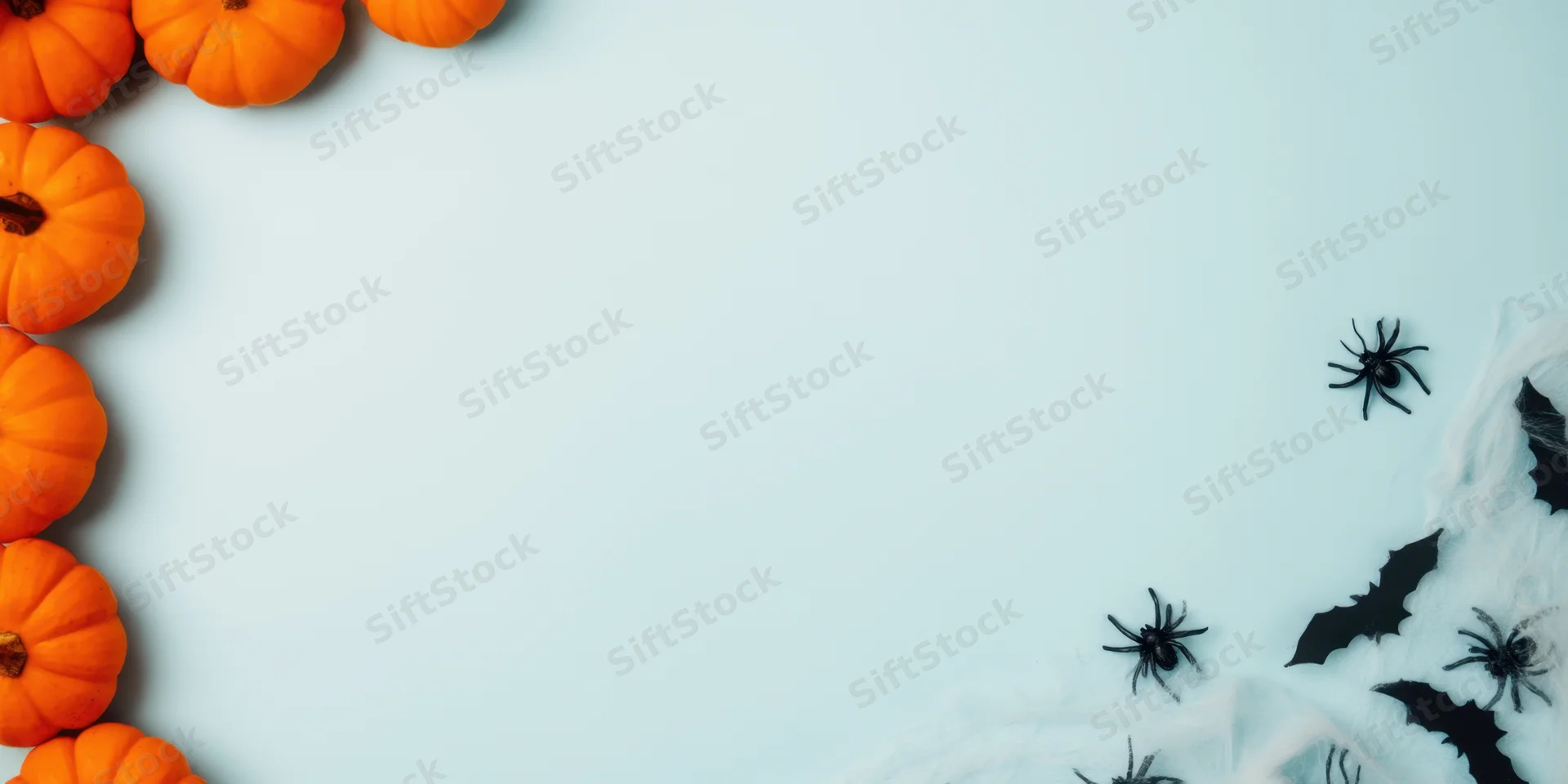 Halloween decor arranged in a flat lay with pumpkins on the left and spiders bats cobwebs on the right on a light blue surface with copyspace