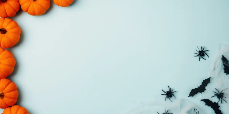 Halloween decor arranged in a flat lay with pumpkins on the left and spiders bats cobwebs on the right on a light blue surface with copyspace