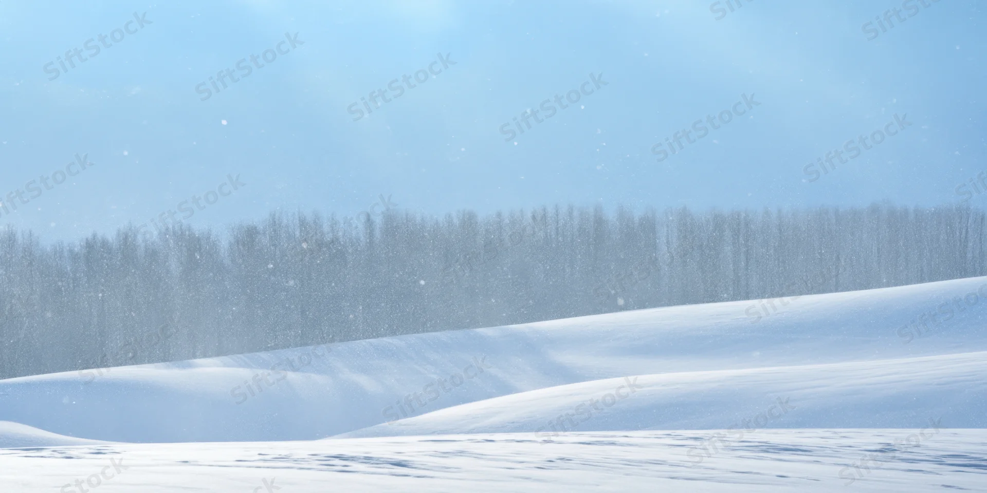 Snow-covered rolling hills under a pale blue sky with falling snow and a distant forest line