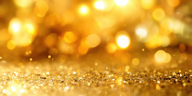 Golden glitter particles scattered across a surface with warm bokeh lights in the background