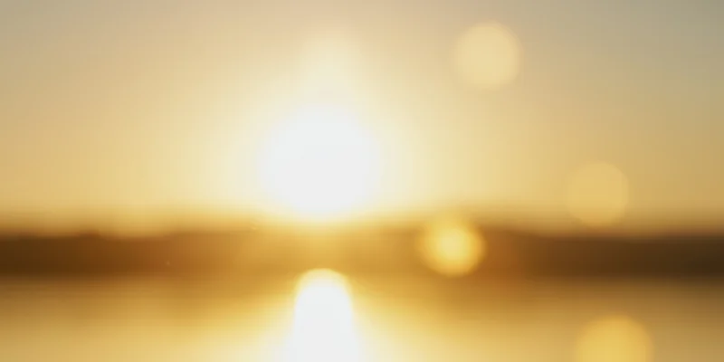 Warm golden sunset over water with soft bokeh reflections and blurred horizon