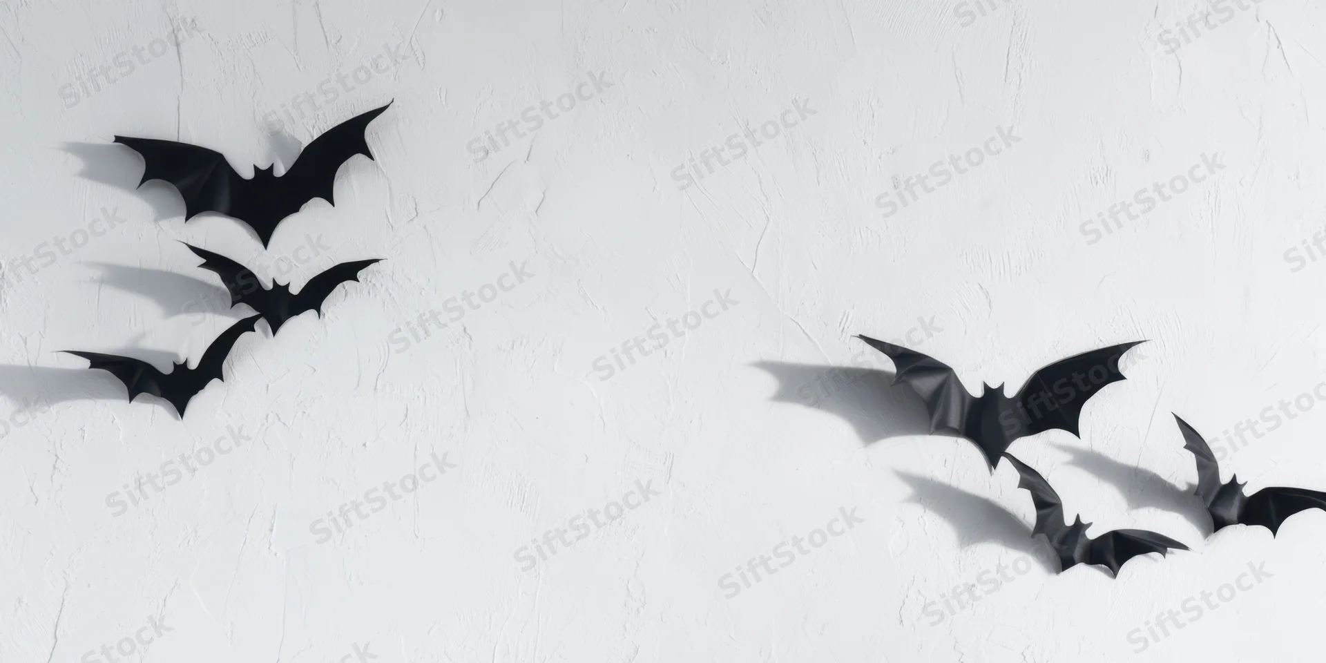 Black paper bats arranged in flight formation on a white textured wall