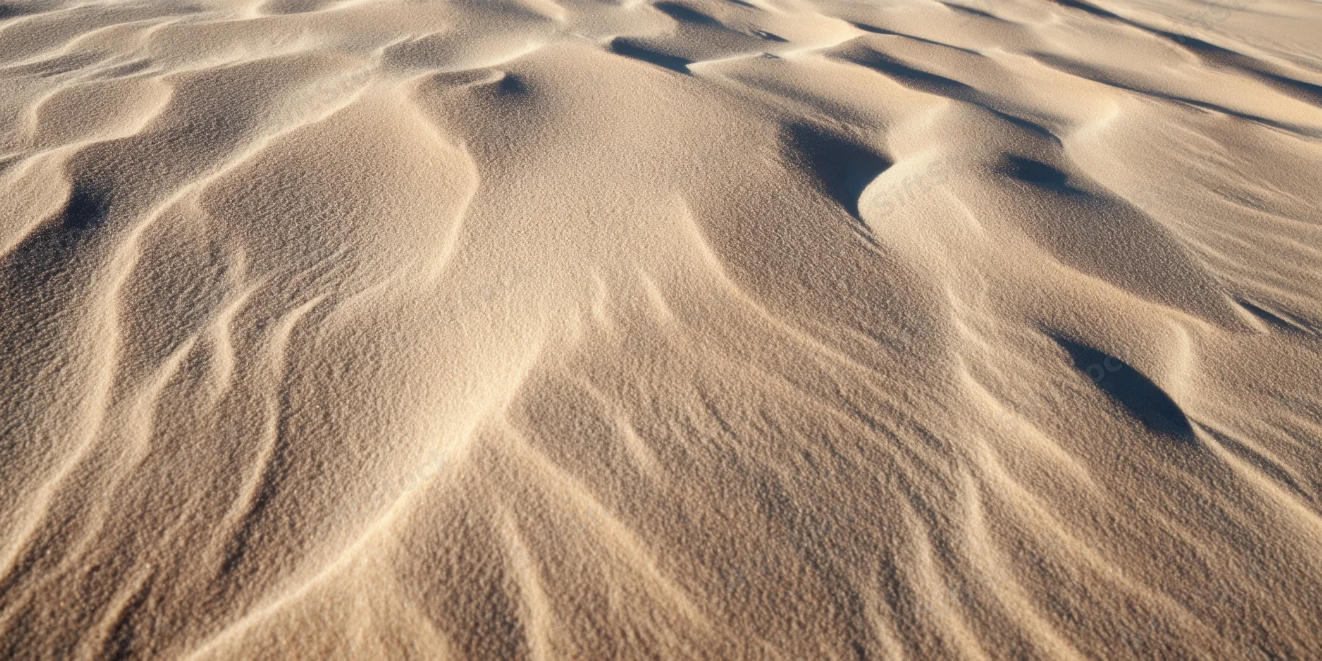 Wind-swept desert sand forming rippled dunes across an arid landscape