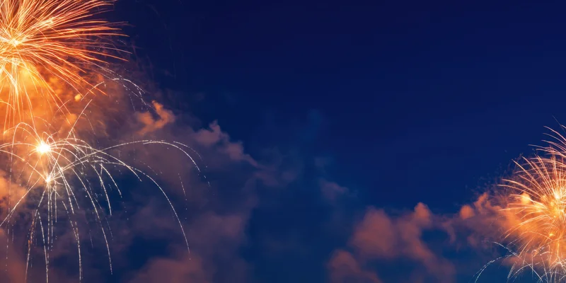Fireworks exploding across deep blue night sky with orange bursts and smoke trails