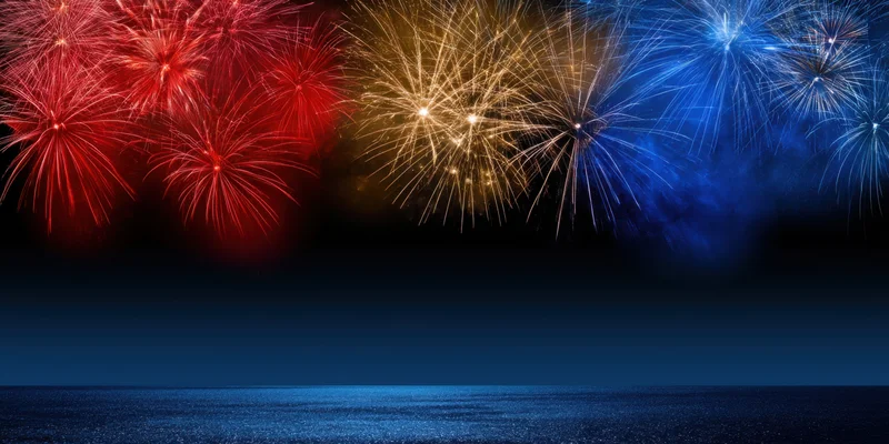 Colorful fireworks bursting overhead over dark ocean at night