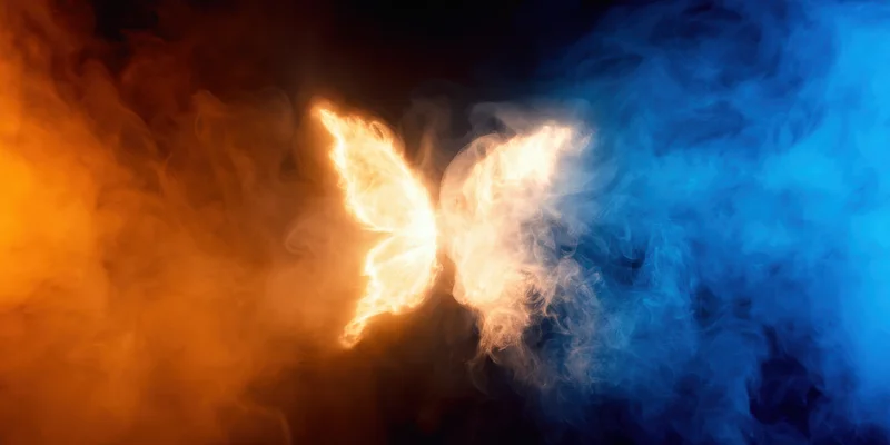 Luminous butterfly formed from orange and blue smoke against dark background