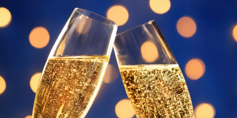 Two champagne flutes clinking with golden bubbles against a blue bokeh light background
