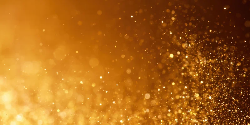 Shimmering gold glitter suspended in air with soft bokeh light effect