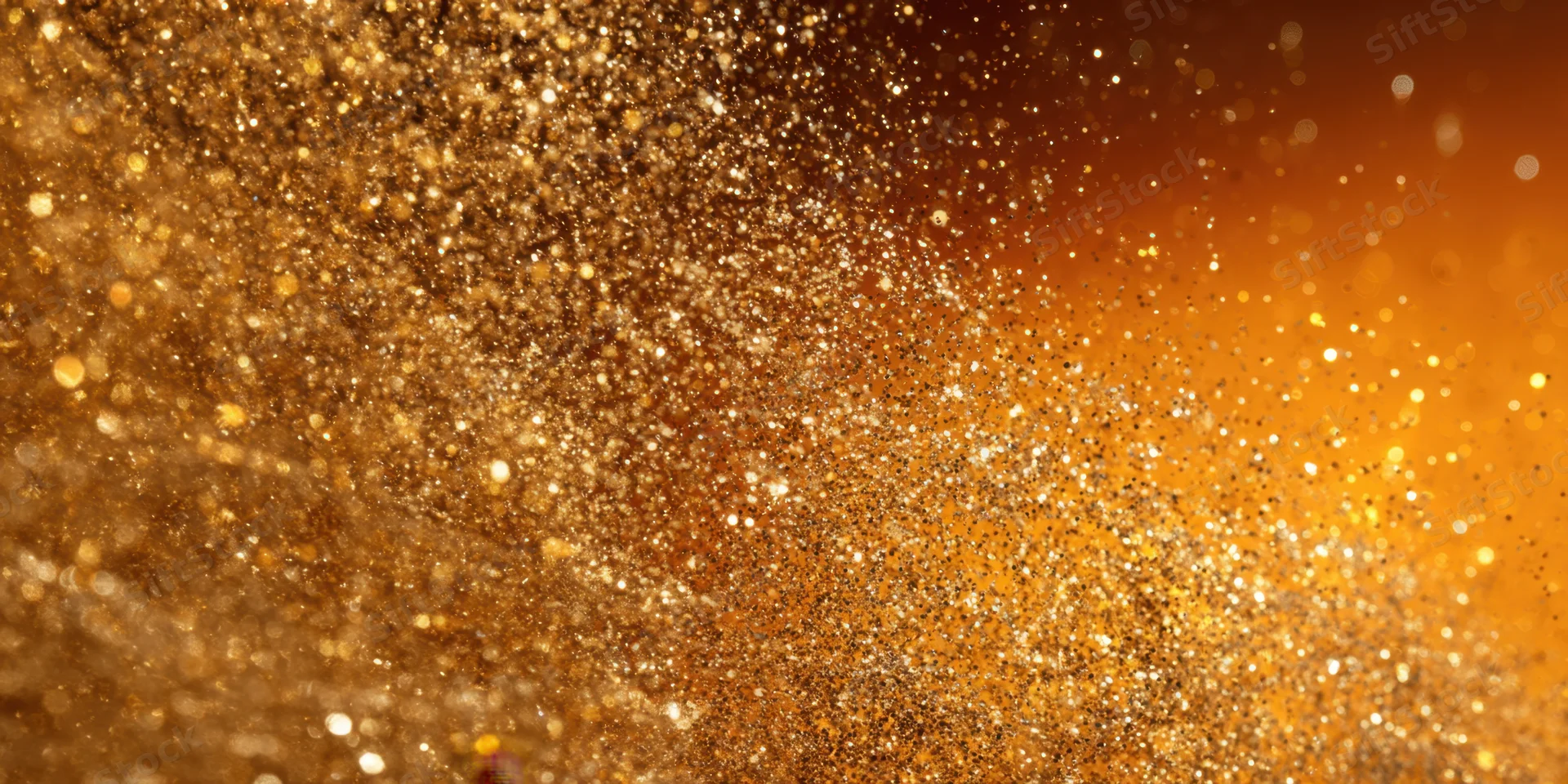 Shimmering gold glitter suspended in air against a warm orange background