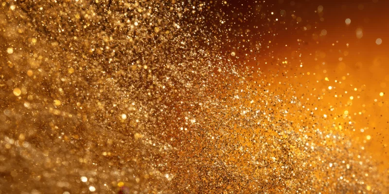Shimmering gold glitter suspended in air against a warm orange background