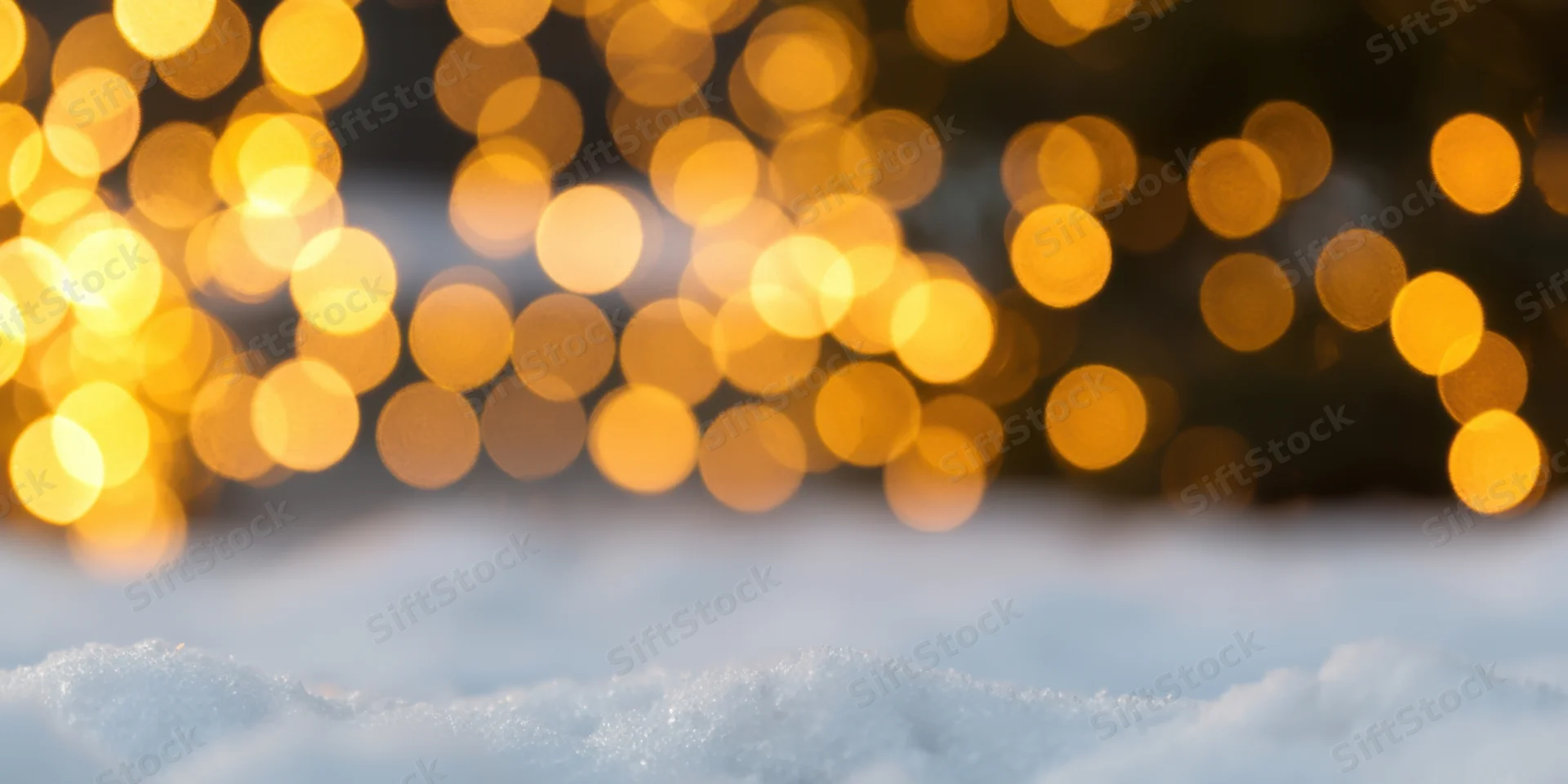 Snow-covered ground in foreground with warm bokeh lights in background