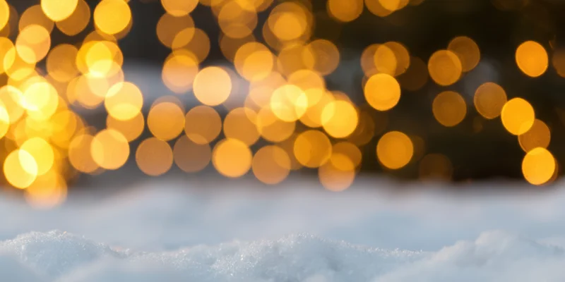 Snow-covered ground in foreground with warm bokeh lights in background
