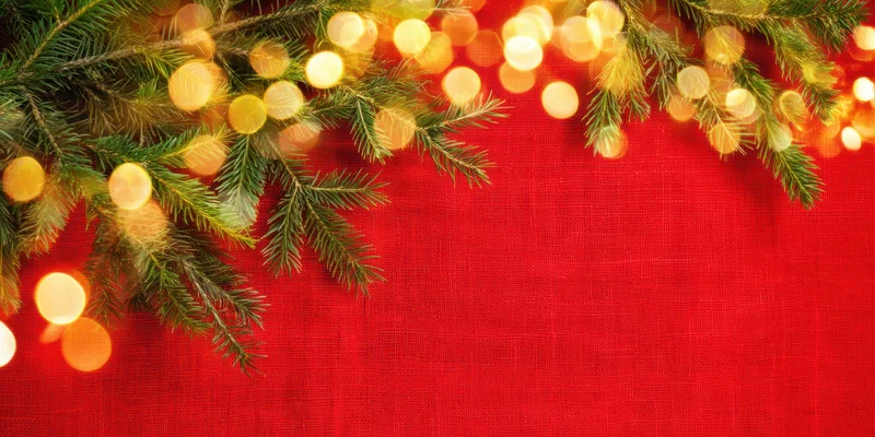Pine branches with warm bokeh lights arranged across red textured linen background