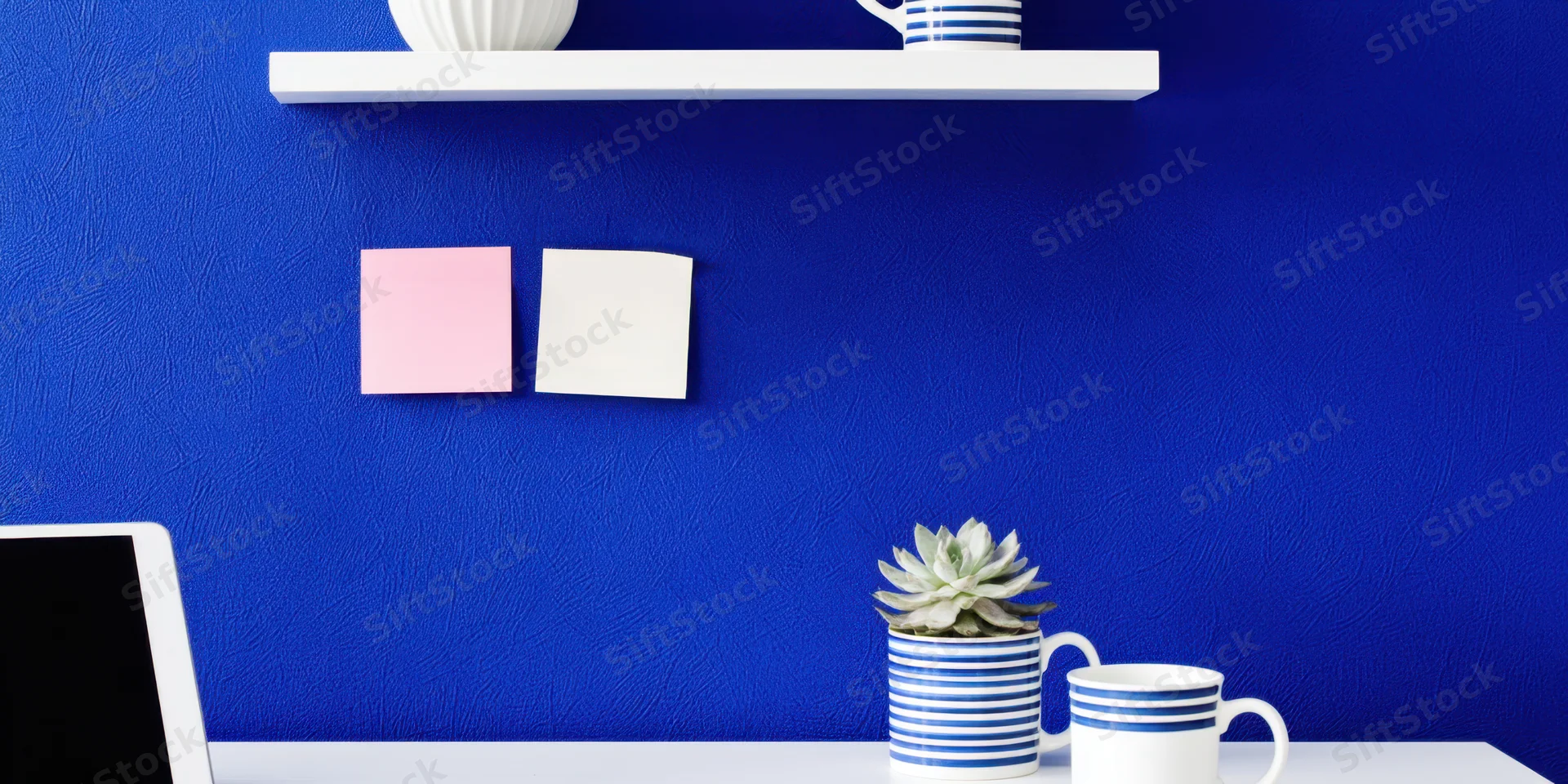 Minimalist desk setup with laptop, succulent, and sticky notes against cobalt blue wall