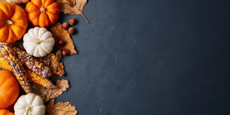 Autumn still life with orange and white pumpkins, dried corn, and fallen leaves arranged on dark stone surface