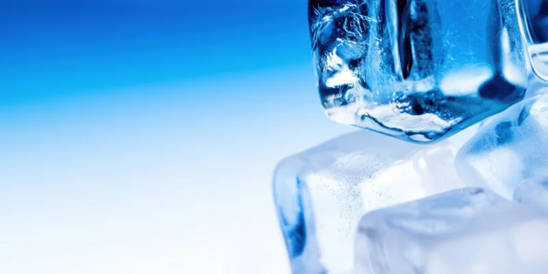 Close-up of clear ice cubes stacked with blue lighting highlighting their facets