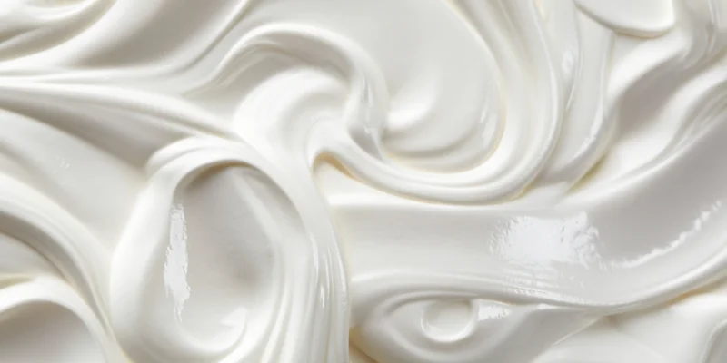 Close-up of smooth white cream with flowing swirls and glossy texture