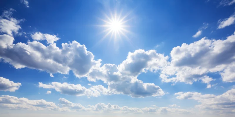Bright sun shining through fluffy white clouds in a clear blue sky