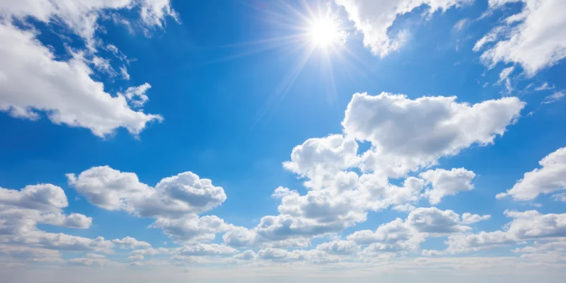 Bright blue sky with fluffy white clouds and sun shining overhead