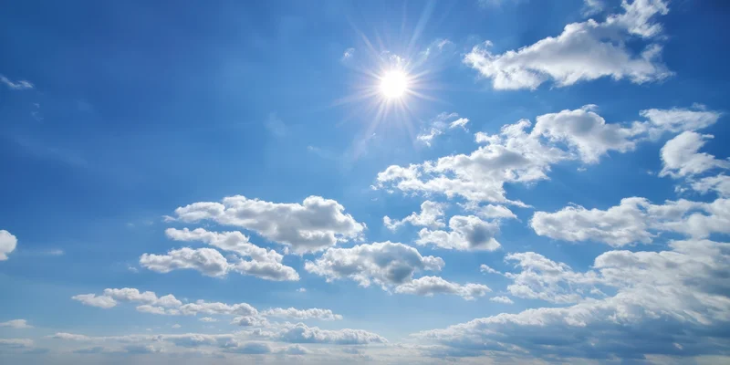 Bright sun shining in a blue sky with scattered fluffy white clouds