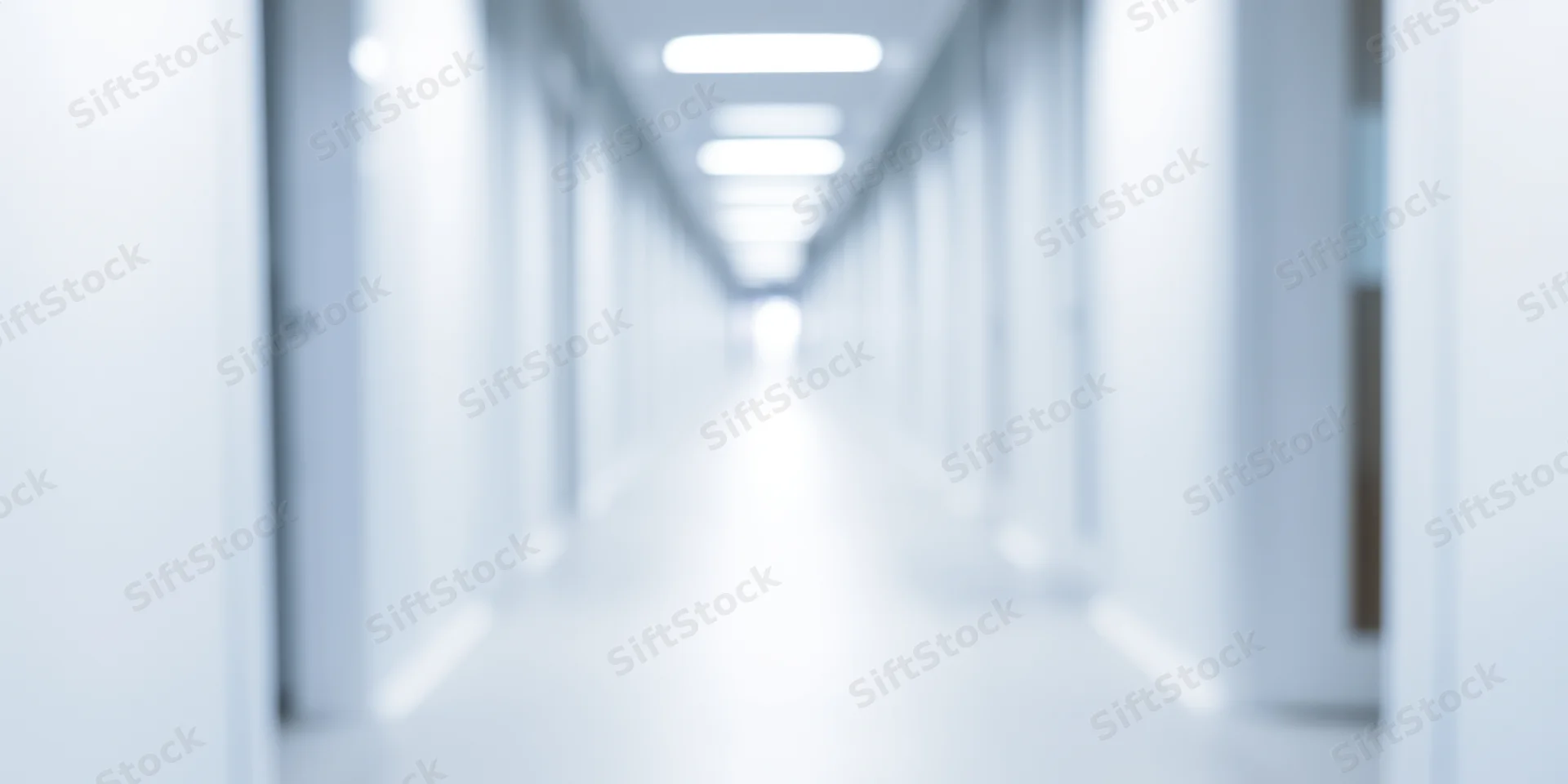 Blurred white corridor with overhead fluorescent lights receding into distance