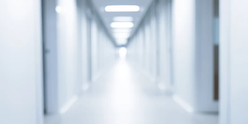 Blurred white corridor with overhead fluorescent lights receding into distance