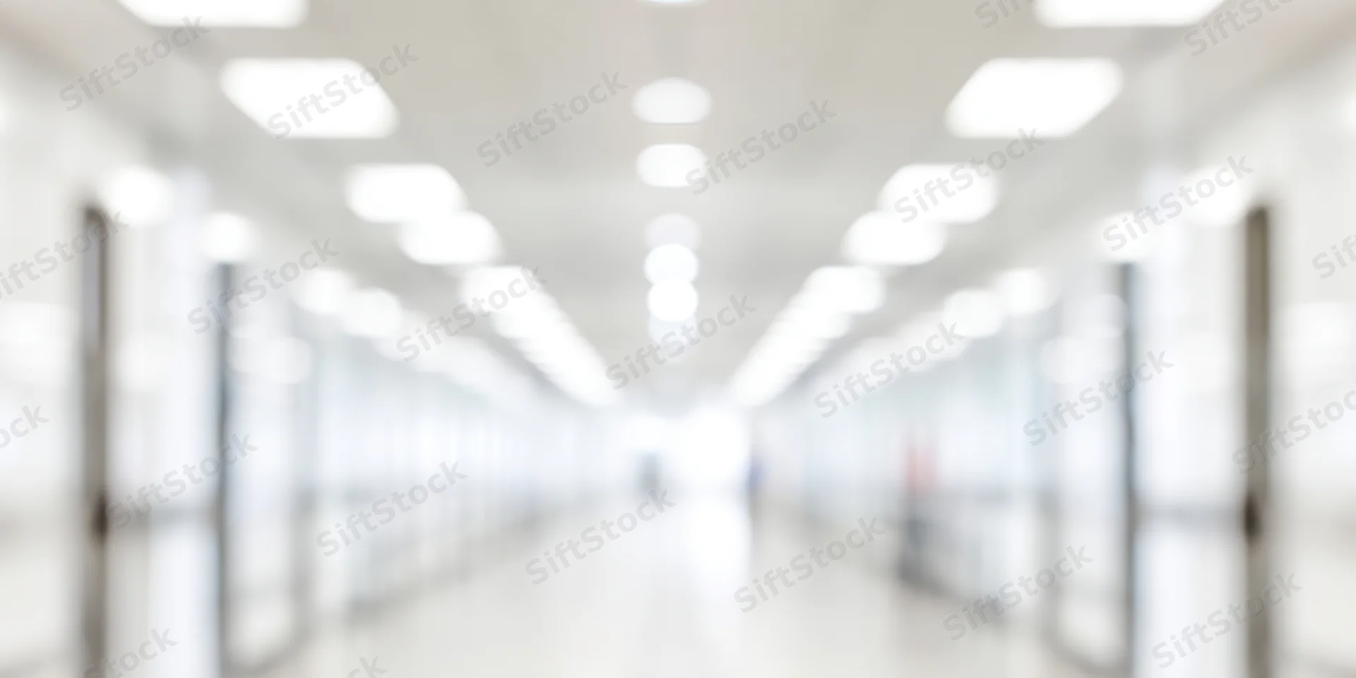Blurred hallway with white walls and overhead lights receding into distance