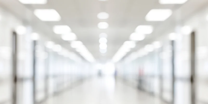 Blurred hallway with white walls and overhead lights receding into distance