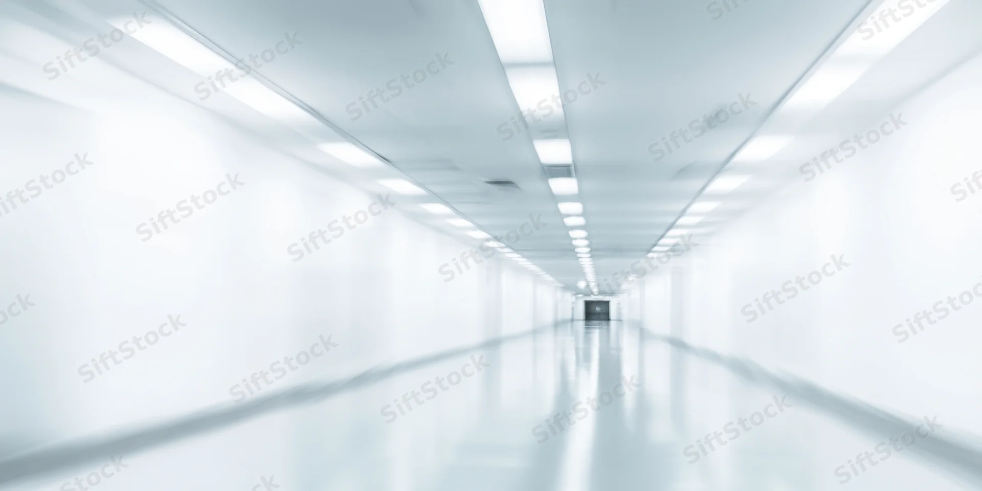 Long white corridor with blurred motion and overhead fluorescent lights receding into distance