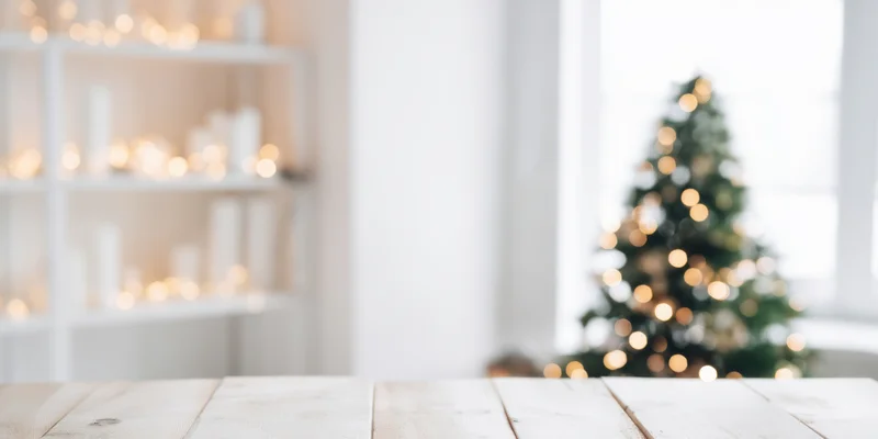 Light wooden table in front of blurred christmas tree and shelves with candles and lights in bright minimalist room
