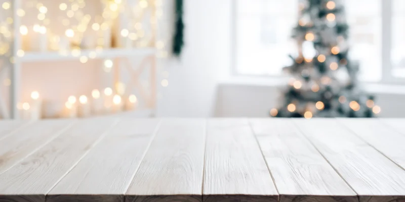 Light wooden table in front of blurred christmas decor with bokeh lights and copyspace