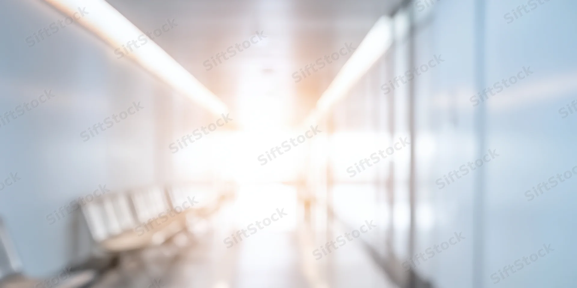 Bright modern corridor with white walls and row of benches leading to light at end
