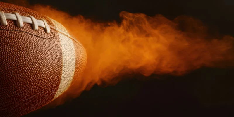 Close-up of an american football with flames trailing behind it against a dark background