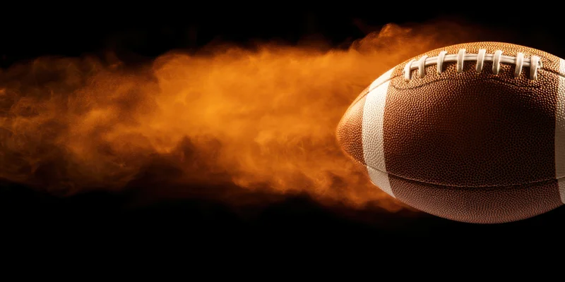 American football in motion with fiery orange smoke trail against black background