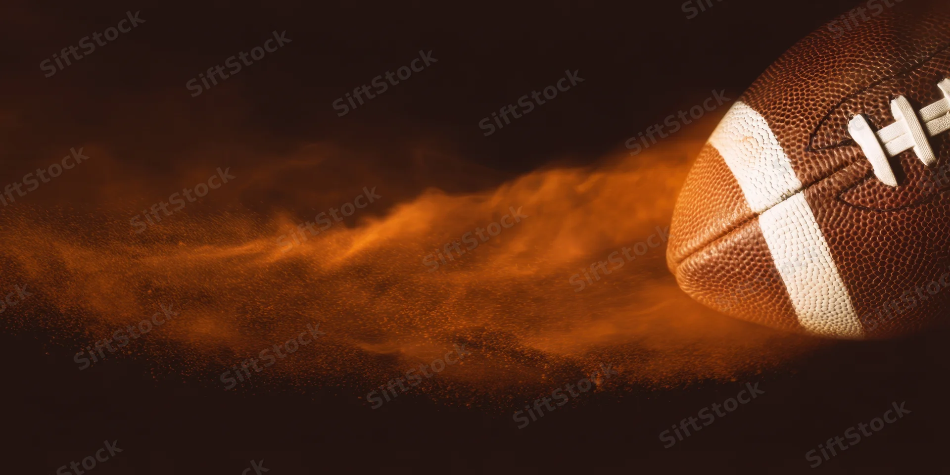 Close-up of an american football with textured brown leather and white laces, surrounded by glowing orange dust in motion against a dark background