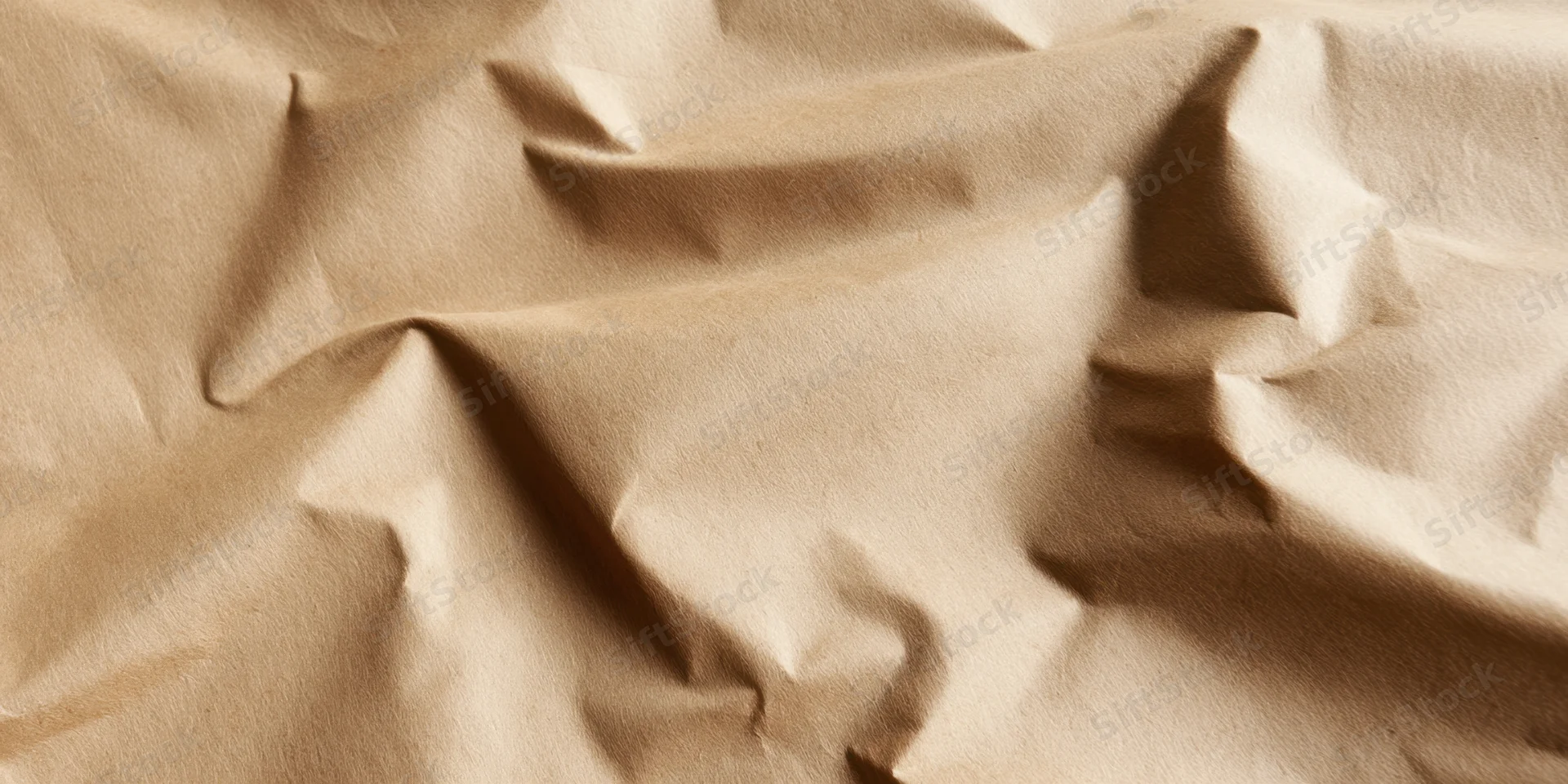 Close-up of crumpled beige kraft paper with deep folds and soft shadows