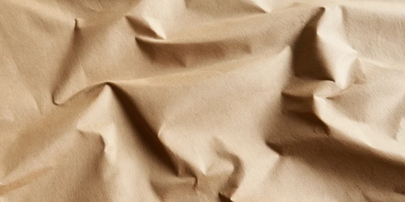 Close-up of crumpled beige kraft paper with deep folds and soft shadows