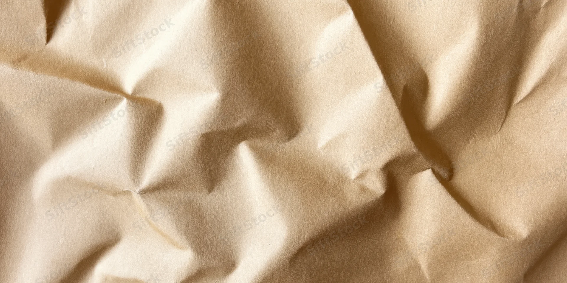 Close-up of crumpled beige kraft paper with deep creases and soft lighting