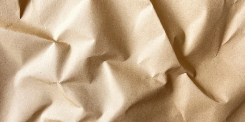 Close-up of crumpled beige kraft paper with deep creases and soft lighting
